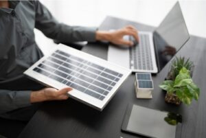 Asesor con portátil sosteniendo panel solar de muestra en oficina; gestión de subvenciones y ayudas para placas solares y autoconsumo en Vitoria-Gasteiz, Álava, País Vasco