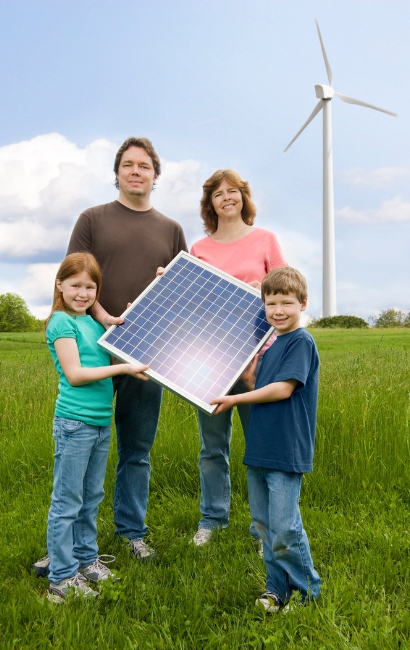 Familia en campo sosteniendo un panel solar con aerogenerador al fondo; reparación de placas solares en Vitoria-Gasteiz, Álava, País Vasco